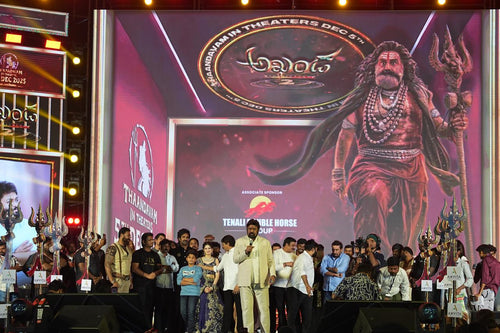 Group of people on a stage with a large screen displaying a movie poster featuring a warrior.