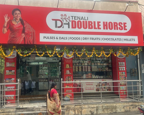 Tenali Double Horse store front with a woman in a red saree waving, decorated with lights.